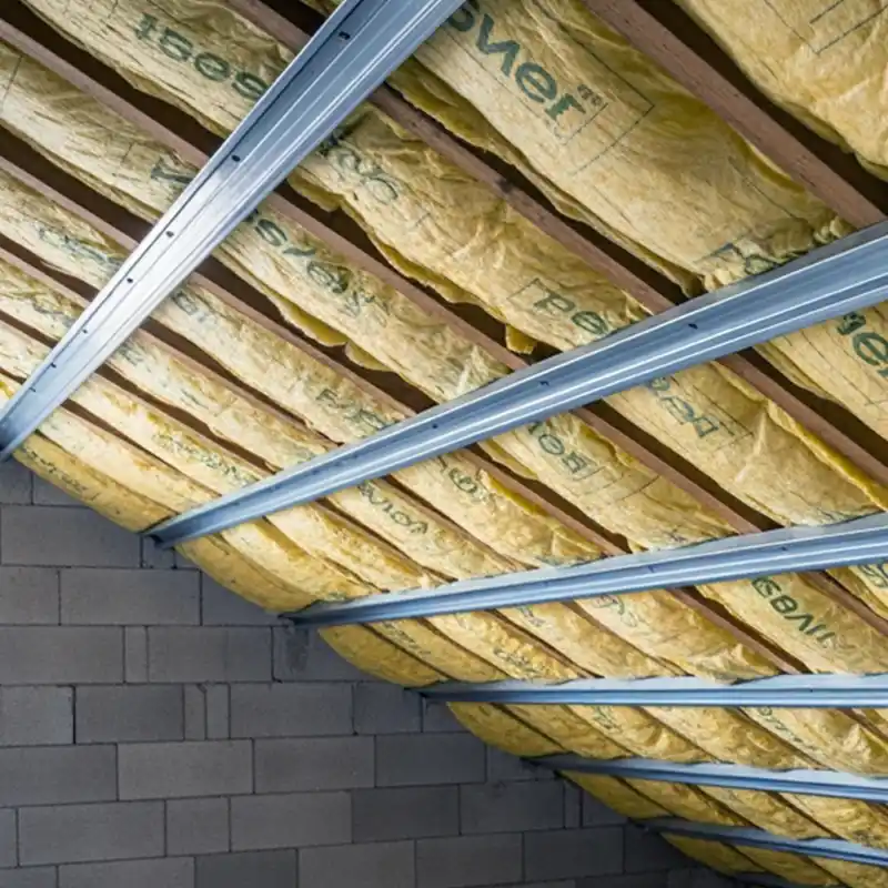 Isolation de toiture 41 Un matériau isolant jaune est installé entre les poutres en bois d'un plafond incliné, soutenu par une ossature métallique. Les murs sont construits en blocs de béton gris, assurant une isolation efficace de toiture dans le 41.